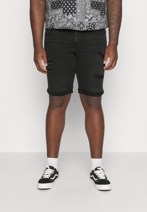 Czarne szorty dżinsowe z przetarciami, z podwiniętymi mankietami i zużytym wyglądem, w połączeniu z czarno-białymi sneakersami i białymi skarpetkami do kostek.