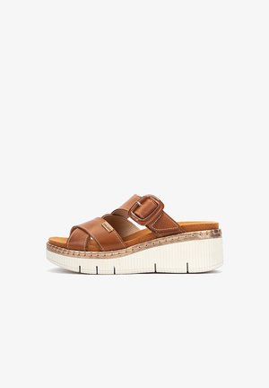 Sandalia de cuero marrón sin cierre con correa ajustable con hebilla, plantilla acolchada y suela plataforma blanca texturizada.