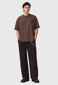 Bruine katoenen t-shirt met een relaxte pasvorm en korte mouwen. Beschikt over een klein zwart logo en contrasterende zwarte broek met een kettingdetail.