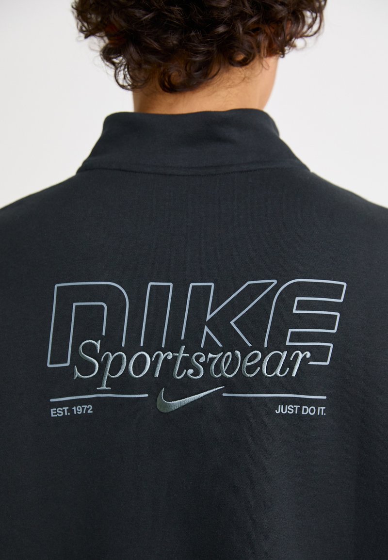 Sudadera negra de Nike Sportswear con logotipo impreso en gris, texto y acentos. Evocadora del estilo deportivo, con un cuello clásico.
