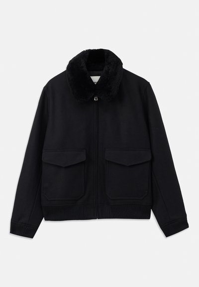 Schwarze Bomberjacke mit einem weichen Kunstfellkragen, Frontreißverschluss und zwei großen aufgesetzten Taschen. Rippbündchen am Saum und an den Ärmeln runden das Design ab.