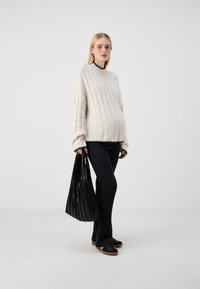 Krämfärgad ribbad tröja med svarta detaljer, svarta tajta byxor och en svart plisserad väska, tillsammans med mörka skor. Enkelt design, mjuk textur.