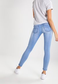 Jeans ajustados de denim azul claro, con una cintura de altura media, dos bolsillos traseros y una textura suave, ligeramente deslavada. Combinados con zapatillas blancas.