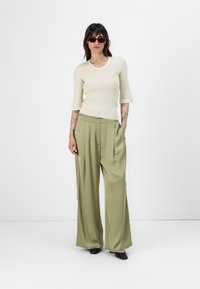 Knit cream top with 3/4 sleeves, paired with wide-leg olive green trousers featuring a button closure and pleated design. Black shoes.