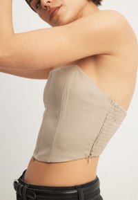 Beež ilma varrukatipp, millel on struktureeritud disain, külgmine smocking detail ja lukuga sulgemine, koos mustade kõrge vöökohaga pükstega.