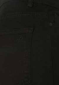 Jeans de mezclilla negra con una textura suave, que presentan un bolsillo trasero y un sutil detalle de logo en relieve. Costuras cosidas y cierre de botón de metal.
