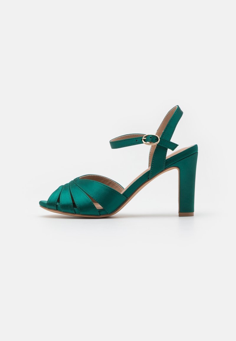 Sandale vert satin à talon haut, bout ouvert, bride à la cheville, boucle dorée et talon bloc sur fond blanc.