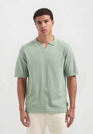 Lichtgroen polo-shirt met korte mouwen, een V-hals kraag en een gladde breisel structuur. Heeft een klein logo-label aan de onderrand.
