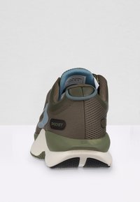 Scarpa sportiva verde e marrone con tomaia in rete, tallone curvo e accenti blu. Presenta un colletto imbottito e il marchio "SHOCKET" sul lato.