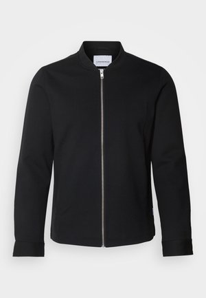 Melnā bomber jakā, kas izgatavota no kokvilnas maisījuma, ir stāvošs apkakle, priekšējā rāvējslēdzēja aizdare un atliekami piedurknes. Gluda tekstūra un minimālistisks dizains.