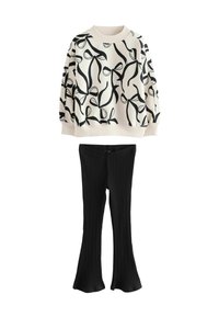 Krämfärgad sweatshirt med svart rosettmönster, ribbade ärmslut; svarta ribbade utsvängda byxor med en åtsittande midja. Koordinerad avslappnad outfit.