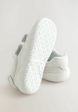 Witte sportieve schoenen met een gestructureerde rubberen zool, een glad bovenwerk, dubbele klittenbandsluitingen en een subtiele grijze accent nabij de hak.