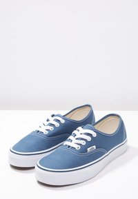 Blue canvas sneakers with white rubber soles and laces. Rounded toe design and contrasting stitching. Logo tag on lateral side.