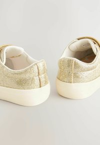 Baskets en paillettes dorées avec une semelle lisse et blanche. La tige texturée présente une finition scintillante et une couture à l'arrière.