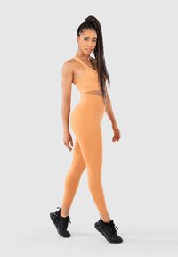 Idrottsset i ljus orange, med en kort topp med nätdetaljer och högmidjade leggings; åtsittande design med slät textur.