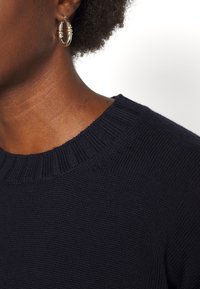 Marineblauer Strickpullover mit geripptem Rundhalsausschnitt, der einen strukturierten Stoff zeigt, sowie eine Nahaufnahme des Kragens und des Schulterbereichs.
