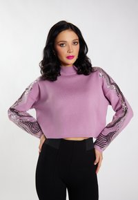Pulover scurt de culoare roz pal cu mâneci lungi, având accente ondulate din paiete negre și argintii. Textură fină de tricot, design cu gât înalt.
