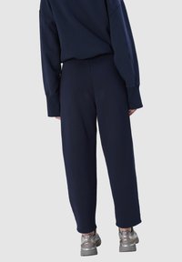 Marineblauwe joggingbroek met een ontspannen pasvorm, voorzien van elastische boorden en een gladde textuur. Gecombineerd met metallic zilveren sneakers.