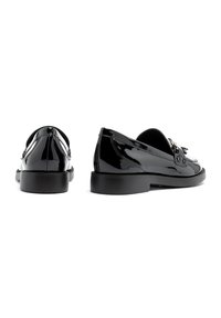 Black patent leather loafers featuring a rounded toe, decorative tassels, and a low, flat rubber sole with minimal detailing.
