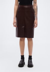 Καφέ δερμάτινη φ ούστα μολύβι με ψηλή μέση, λεία υφή, εμπρόσθιες ραφές και πλαϊνές τσέπες, συνδυασμένη με μαύρα loafers και κάλτσες.