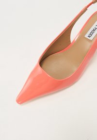 Décolleté slingback in vernice corallo, con punta affusolata e tacco slanciato, dotato di una parte posteriore per una vestibilità e un supporto ottimali.