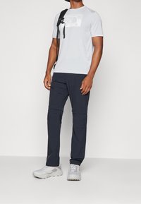 Ljusgrå t-shirt med kort ärm och North Face-logga, matchad med mörkblå cargobyxor med blixtlåsfickor och ljusgrå sportskor.