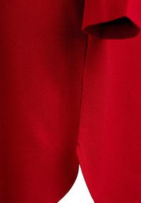 Primer plano de una tela texturizada de color rojo brillante con una costura y una esquina doblada, destacando los detalles del material y la costura.