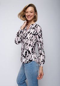 Chemisier à manches longues en tissu noir avec un grand motif de texte "love" en blanc et rose. Il dispose d'un col à boutons et d'une coupe décontractée.