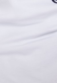 Weißer Baumwoll-T-Shirt-Stoff mit glatter Textur, versehen mit dunkel bedrucktem Schriftzug. Keine sichtbaren Muster oder Hardware-Details.