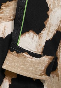 Tessuto a stampa bovina nero e beige con aree testurizzate. Presenta un accento verde a contrasto e cuciture nere lungo l'orlo e il bordo.
