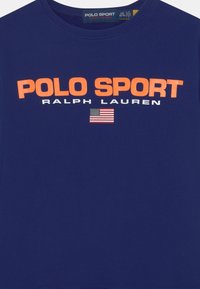 Mörkblå bomullströja med fet orange text "POLO SPORT" och "RALPH LAUREN", samt en liten amerikansk flagga nedanför. Rund halsringning.