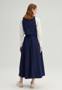 Robe en coton marine avec un corsage ajusté, une taille cintrée et une jupe fluide. Manches longues blanches, accents de boutons sur les poignets et texture subtile.