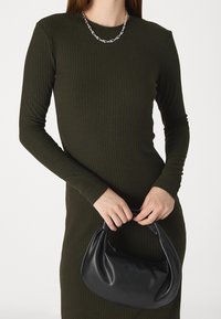 Šaty s dlouhým rukávem a žebrovaným vzorem v tmavě olivové barvě, doplněné černou koženou kabelkou s měkkou texturou a uzlem na rukojeti.