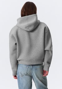 Harmaa lyhyt huppari pehmeästä kankaasta, jossa on huppu, resorit hihansuissa ja yksinkertainen muotoilu. Yhdistetty vaaleansinisiin farkkuihin.