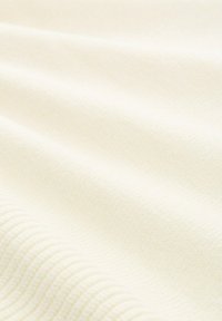 Tessuto color bianco sporco con superficie morbida e testurizzata e un design sottile a coste. Le pieghe creano ombre delicate, valorizzando la profondità del materiale.