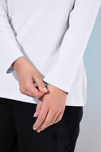 Osoba nosząca białą koszulę z długim rękawem i czarne spodnie, jedna ręka delikatnie trzyma nadgarstek drugiej dłoni.