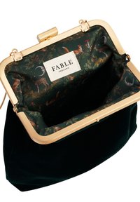 Green velvet clutch bag with gold-tone metal clasp, featuring a patterned interior showcasing forest animals. Label reads "FABLE ENGLAND."