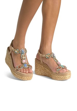 Beige wedge sandals with woven jute soles, embellished with colorful gem accents and a T-strap design. Open toe and ankle buckle closure.