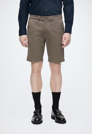 Muž oblečený v hnedých krátkych nohaviciach po kolená, čiernych ponožkách, čiernych spoločenských topánkach a tmavomodrej košeli s dlhým rukávom na gombíky.