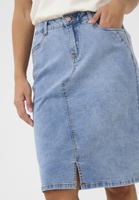 Džínová sukně světle modré barvy se rovnou siluetou, předním rozparkem, viditelnými švy a kapsami. Zapínání na knoflík v pase.