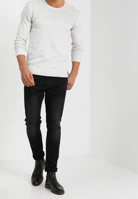 Maglione lavorato a maglia grigio chiaro con trama a coste, abbinato a jeans neri aderenti e stivaletti neri in pelle.