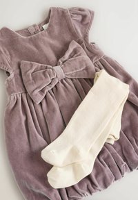 Samtkleid in gedämpftem Lila mit einer großen vorderen Schleife und einem plissierten Rock, kombiniert mit cremefarbenen gerippten Strumpfhosen. Sanfte, weiche Textur.