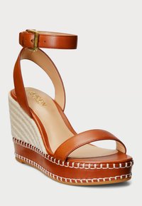 Sandalo wedge in pelle marrone con cinturino alla caviglia, dettaglio in juta intrecciata e cuciture bianche sulla piattaforma. Texture liscia con design a punta arrotondata.