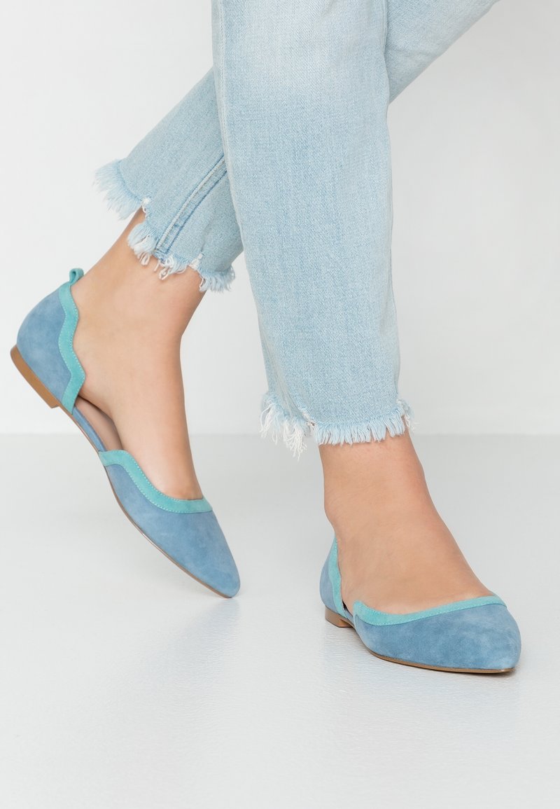 Dwukolorowa para płaskich butów z miękkiego zamszu w jasnoniebieskim i teal, z falbaniastym brzegiem i małym obcasem z tyłu.