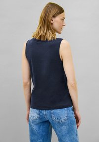 Top senza maniche blu navy in tessuto morbido, con scollatura rotonda e vestibilità comoda, abbinato a jeans di denim azzurro.