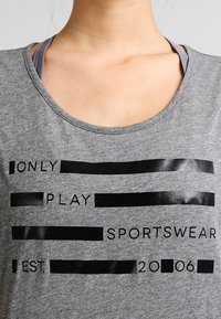 Close-up of a gray sportswear shirt with black printed text partially obscured by black bars over some words.
