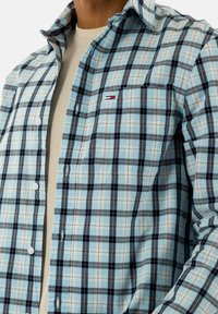 Heren overhemd met knopen in lichtblauw ruitpatroon met donkerblauwe en zwarte vierkanten. Heeft één borstzak en contrasterende stiksels.