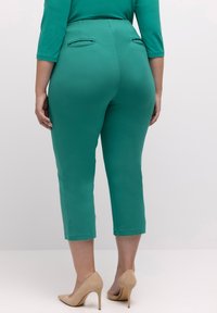 Vihreät capri-housut, jotka on valmistettu sileästä kankaasta, ja niissä on kaksi takataskua sekä keski-korkea vyötärö. Yhdistettynä nude-väriin korkokenkiin.