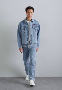 Lichtblauwe denimjas met twee borstzakken, gecombineerd met bijpassende lichtblauwe spijkerbroek en witte sneakers. Eenvoudig, casual ontwerp.