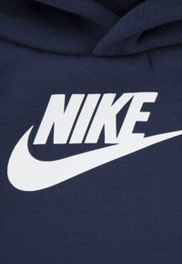 Felpa con cappuccio blu navy caratterizzata da un grande logo Nike bianco e dal suo iconico baffo su un tessuto morbido e testurizzato.